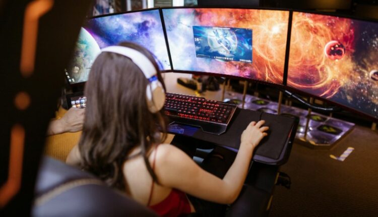 Woman with headphones playing on a multi-screen gaming setup featuring vibrant space imagery., tags: eingabe-automatisierung - pexel