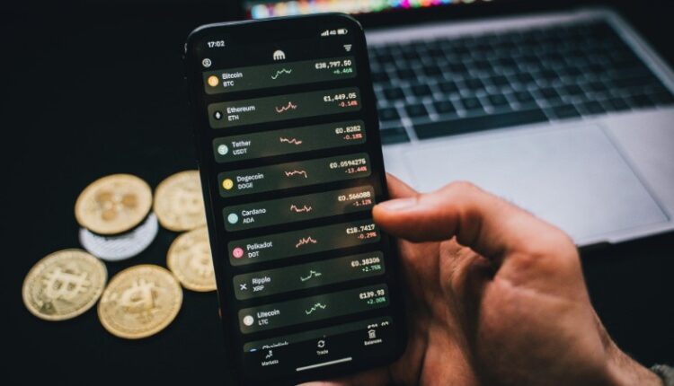 A person checks cryptocurrency values on a smartphone with a laptop and Bitcoins nearby., tags: casinos und - pexel