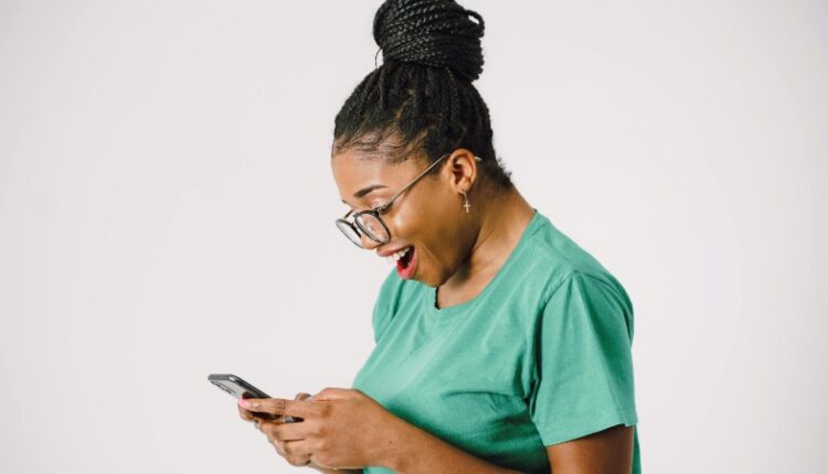 Woman wearing glasses, excitedly texting on smartphone while standing indoors., tags: für - pexel