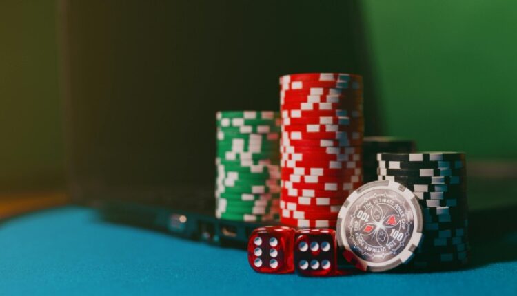 Close-up of casino chips and dice on a felt table, next to a laptop for online gambling., tags: neue - pexel